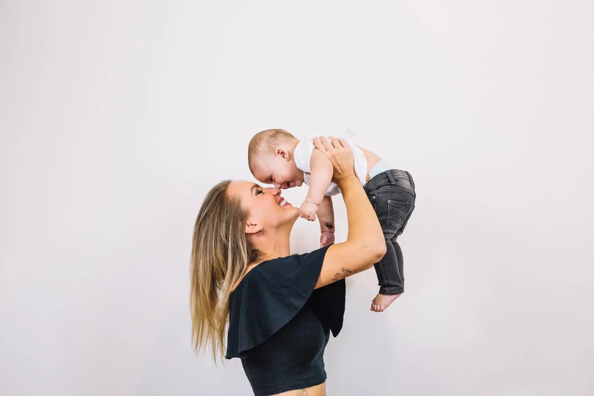 Photo of a mother wearing a black top holding her child up, wondering "What is a Mommy Makeover?"
